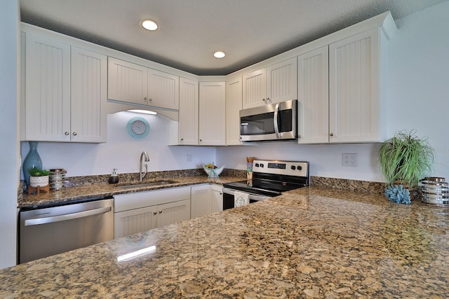 kitchen with sink, stainless steel appliances, white cabinets, and dark stone countertops