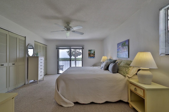 bedroom with a textured ceiling, access to exterior, light colored carpet, two closets, and ceiling fan