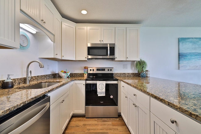 kitchen featuring dark stone counters, white cabinets, appliances with stainless steel finishes, light hardwood / wood-style floors, and sink