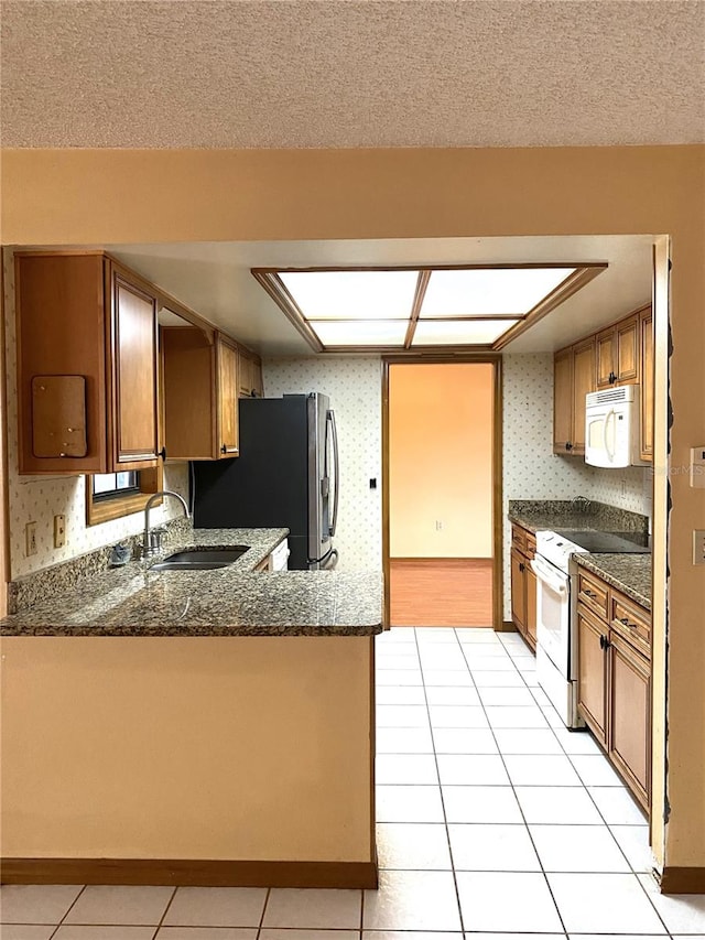 kitchen featuring white appliances, light tile patterned floors, sink, kitchen peninsula, and dark stone counters