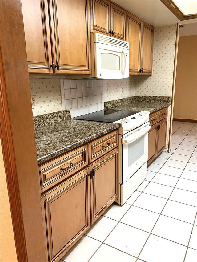 kitchen featuring white appliances, light tile patterned floors, dark stone counters, and tasteful backsplash