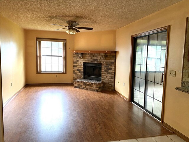 unfurnished living room featuring ceiling fan, plenty of natural light, a textured ceiling, and a brick fireplace