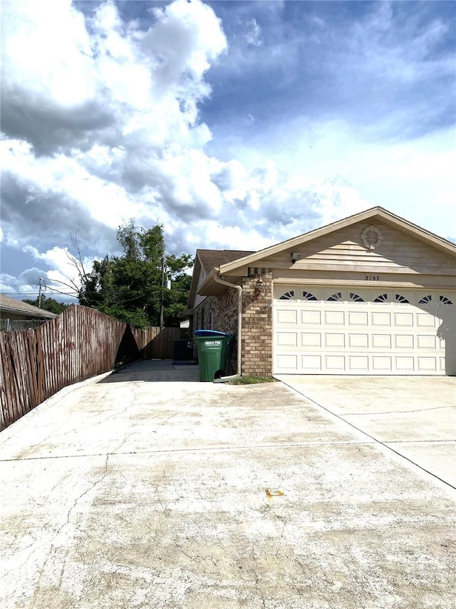 view of side of property with a garage, fence, concrete driveway, and brick siding