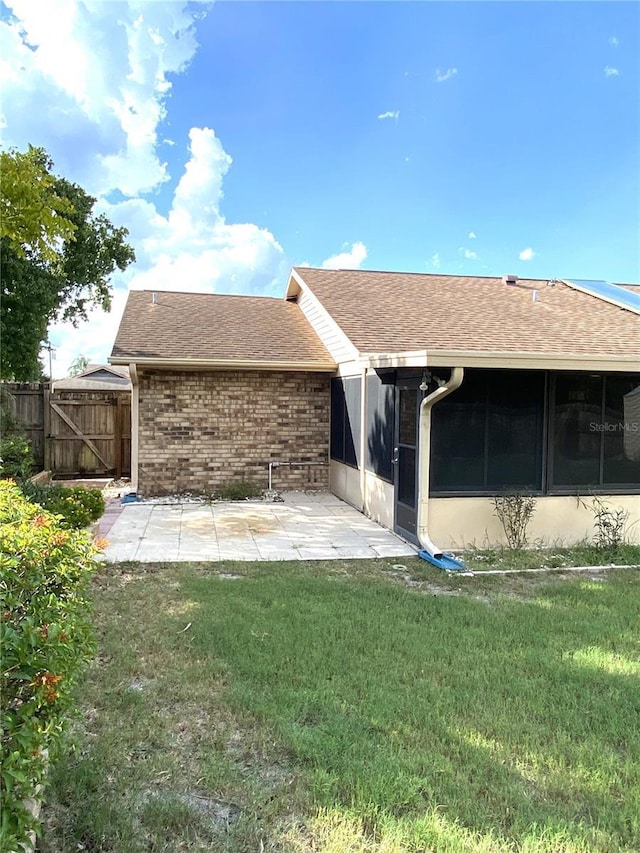 back of property with a sunroom, a lawn, and a patio