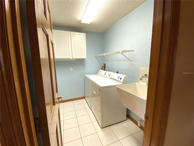 laundry room with a textured ceiling, light tile patterned floors, sink, washer and dryer, and cabinets