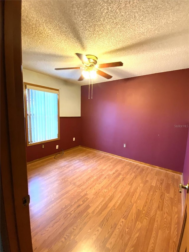 unfurnished room with ceiling fan, a textured ceiling, and light wood-type flooring