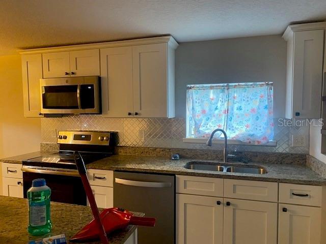 kitchen featuring appliances with stainless steel finishes, white cabinets, sink, backsplash, and stone countertops