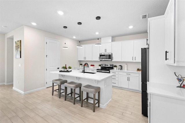 kitchen featuring pendant lighting, an island with sink, sink, white cabinets, and stainless steel appliances