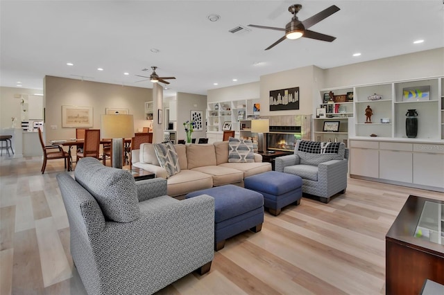 living room featuring ceiling fan, a tiled fireplace, and light hardwood / wood-style floors