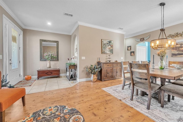 dining space with a textured ceiling, a chandelier, light hardwood / wood-style floors, and crown molding