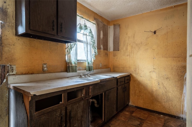 kitchen with a textured ceiling, dark brown cabinets, and sink