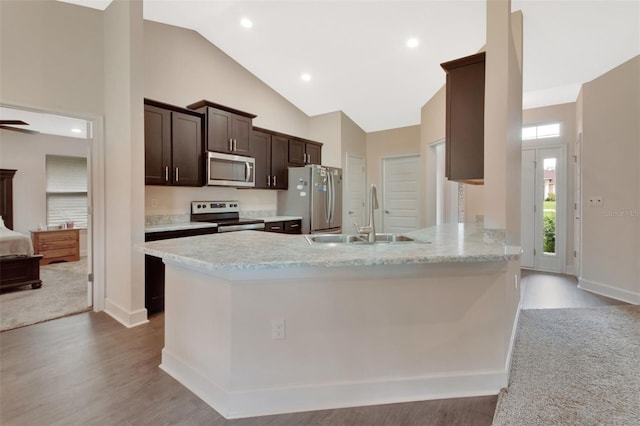 kitchen featuring appliances with stainless steel finishes, high vaulted ceiling, sink, light hardwood / wood-style floors, and kitchen peninsula