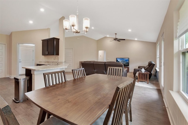 dining area with ceiling fan with notable chandelier, lofted ceiling, sink, and light hardwood / wood-style flooring