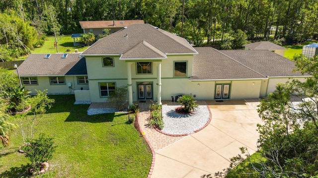 view of front of home with a shingled roof, a front yard, driveway, and stucco siding