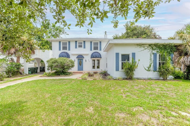 view of front of house with concrete driveway, a chimney, french doors, a front lawn, and stucco siding