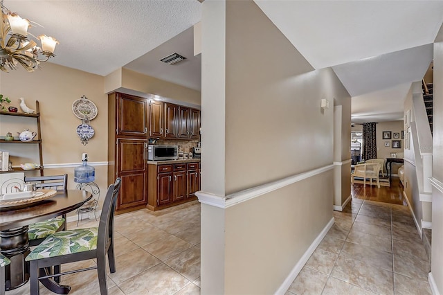 kitchen featuring an inviting chandelier, light tile patterned floors, decorative backsplash, and a textured ceiling