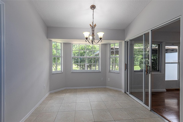 unfurnished room featuring a textured ceiling, light tile patterned floors, and an inviting chandelier