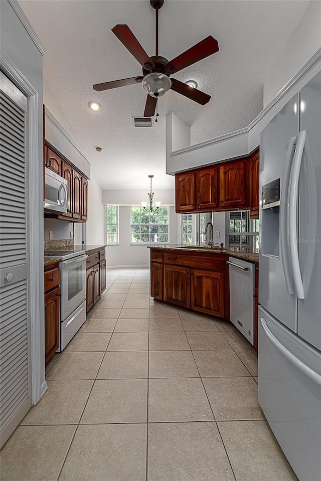 kitchen featuring light tile patterned floors, kitchen peninsula, ceiling fan with notable chandelier, appliances with stainless steel finishes, and pendant lighting