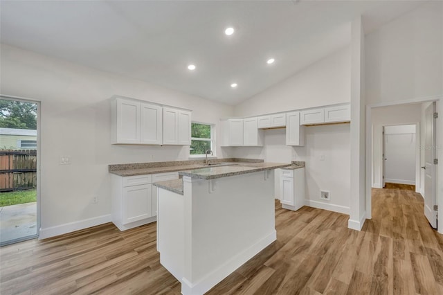 kitchen with light wood-type flooring, white cabinets, a kitchen island, sink, and high vaulted ceiling