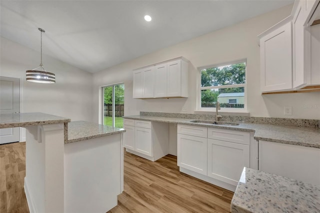 kitchen featuring white cabinetry, hanging light fixtures, a healthy amount of sunlight, sink, and light hardwood / wood-style flooring