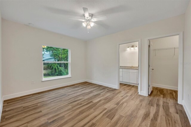 unfurnished bedroom featuring ensuite bathroom, light hardwood / wood-style flooring, a closet, a walk in closet, and ceiling fan