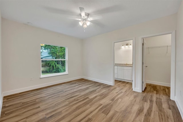 unfurnished bedroom with ensuite bath, light hardwood / wood-style flooring, ceiling fan, a walk in closet, and a closet