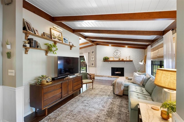 living room featuring dark wood-type flooring, vaulted ceiling with beams, a brick fireplace, and brick wall