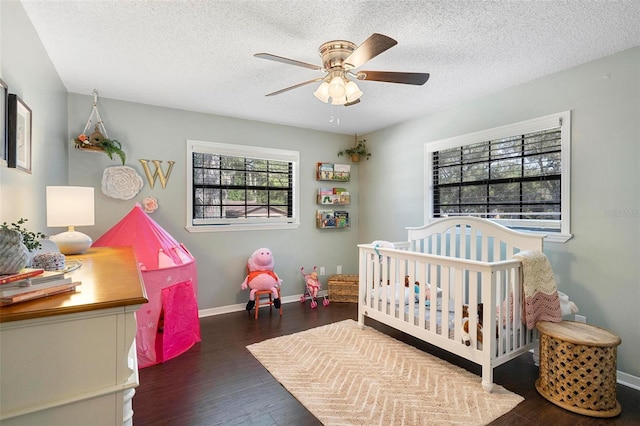 bedroom featuring dark hardwood / wood-style flooring, a textured ceiling, a crib, and ceiling fan