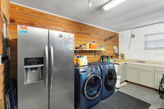 laundry room featuring washing machine and clothes dryer, wood walls, cabinets, and a textured ceiling