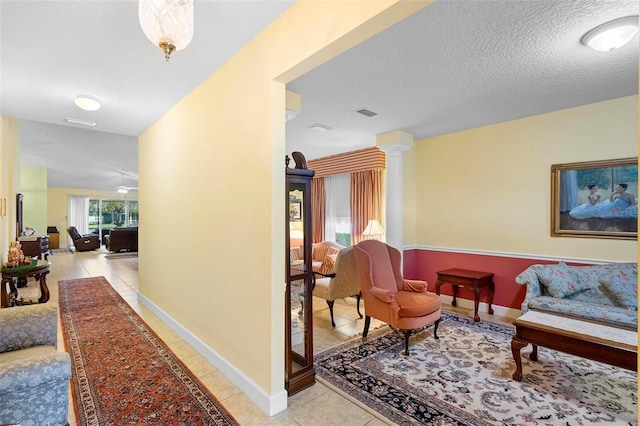 hall with light tile patterned floors, decorative columns, and a textured ceiling