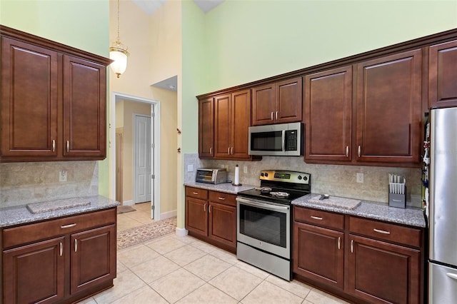 kitchen featuring light tile patterned floors, appliances with stainless steel finishes, light stone countertops, and decorative backsplash