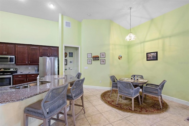 kitchen featuring sink, hanging light fixtures, stainless steel appliances, a kitchen bar, and dark stone counters