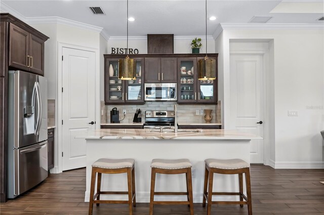 kitchen featuring dark wood-type flooring, pendant lighting, a kitchen island with sink, appliances with stainless steel finishes, and tasteful backsplash