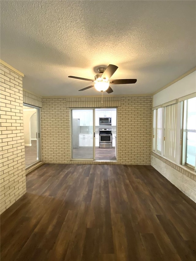 unfurnished living room with a textured ceiling, dark wood-type flooring, ceiling fan, and brick wall