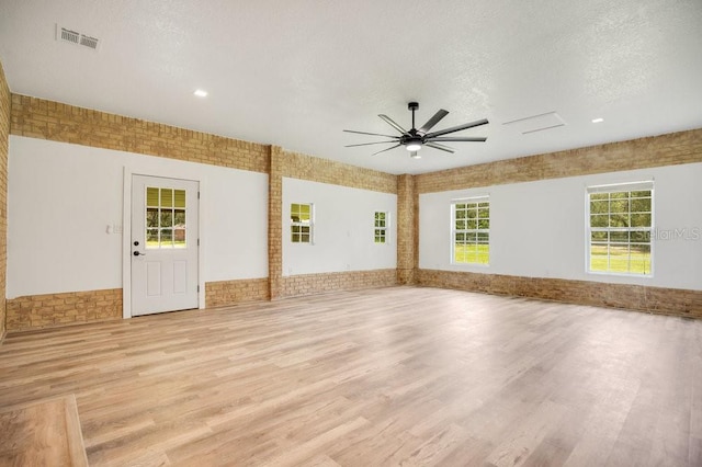 empty room with ceiling fan, light hardwood / wood-style floors, brick wall, and a textured ceiling