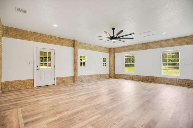 unfurnished room with light wood finished floors, visible vents, a ceiling fan, a textured ceiling, and brick wall