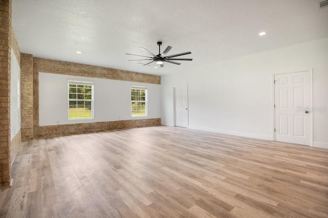 unfurnished living room with light hardwood / wood-style floors, brick wall, a textured ceiling, and ceiling fan