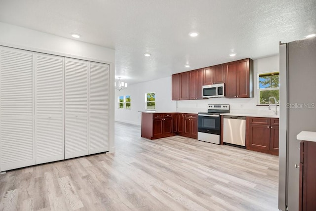 kitchen featuring appliances with stainless steel finishes, light countertops, a textured ceiling, light wood-style floors, and a sink