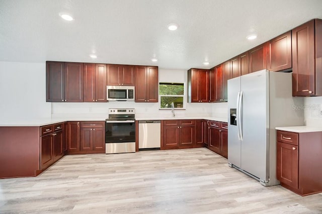 kitchen with stainless steel appliances, sink, light wood-type flooring, and a textured ceiling