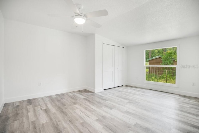 unfurnished bedroom featuring lofted ceiling, a textured ceiling, ceiling fan, light hardwood / wood-style floors, and a closet