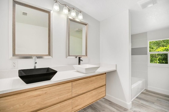 bathroom with shower / bath combination, a textured ceiling, hardwood / wood-style floors, and double sink vanity