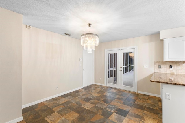 unfurnished dining area with french doors, a textured ceiling, and an inviting chandelier