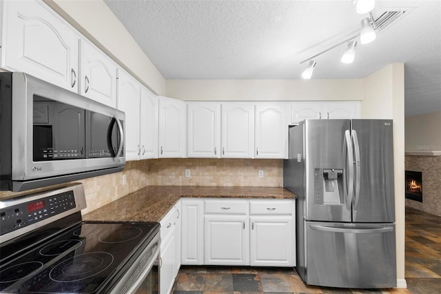 kitchen featuring appliances with stainless steel finishes, tasteful backsplash, dark stone counters, a textured ceiling, and white cabinetry