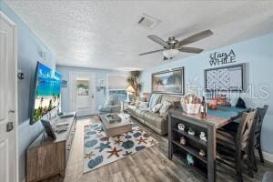 living room featuring wood-type flooring, a textured ceiling, and ceiling fan