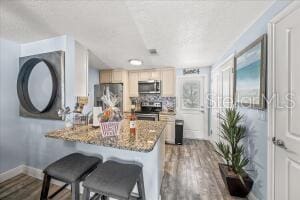 kitchen featuring a breakfast bar, dark stone counters, hardwood / wood-style floors, appliances with stainless steel finishes, and light brown cabinetry