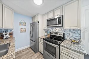 kitchen featuring light wood-type flooring, white cabinets, light stone counters, stainless steel appliances, and decorative backsplash