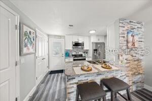 kitchen with a breakfast bar, white cabinets, dark hardwood / wood-style floors, appliances with stainless steel finishes, and sink