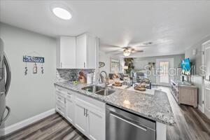 kitchen with white cabinets, kitchen peninsula, stainless steel dishwasher, light stone countertops, and ceiling fan