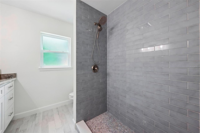 bathroom featuring vanity, hardwood / wood-style flooring, toilet, and tiled shower