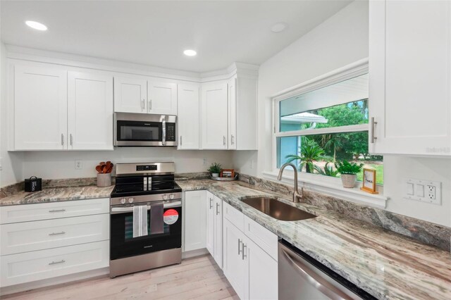 kitchen featuring white cabinets, light stone countertops, light wood-type flooring, sink, and stainless steel appliances